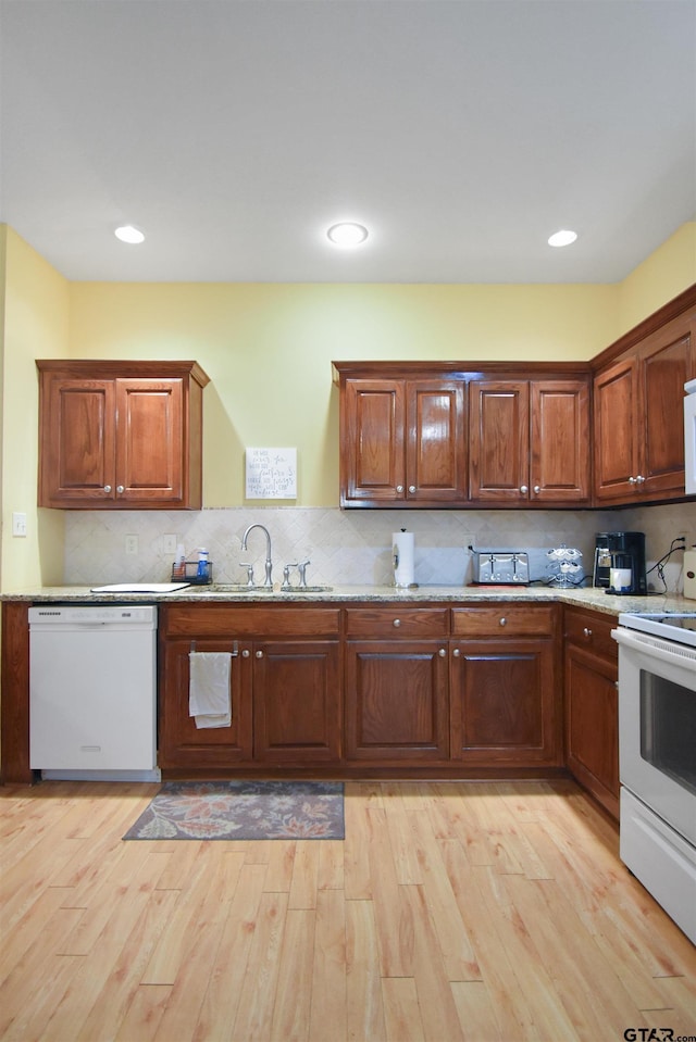 kitchen featuring white appliances, a sink, tasteful backsplash, and light wood finished floors