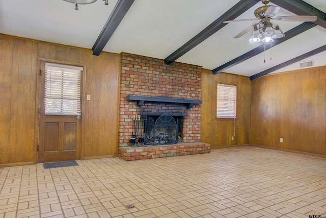 unfurnished living room featuring a healthy amount of sunlight, a brick fireplace, lofted ceiling with beams, and wooden walls