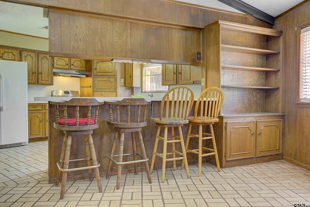 kitchen featuring a kitchen bar, white fridge, kitchen peninsula, and ornamental molding