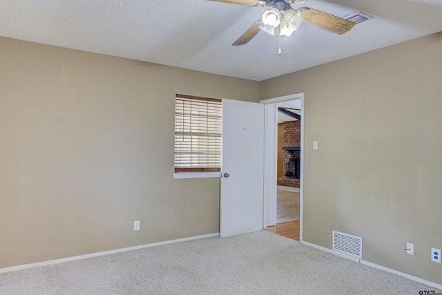 carpeted spare room featuring a textured ceiling, ceiling fan, and a brick fireplace