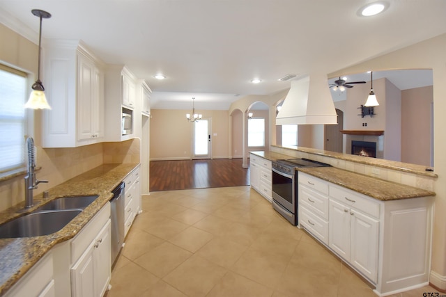 413 Maggie Cir, Flint, TX 75762 - kitchen featuring appliances with stainless steel finishes, custom exhaust hood, ceiling fan, a warm lit fireplace, and white cabinetry