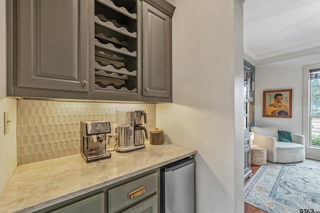 bar with gray cabinets, refrigerator, tasteful backsplash, light stone countertops, and ornamental molding