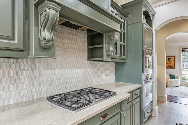 kitchen featuring light tile patterned flooring, appliances with stainless steel finishes, backsplash, light stone counters, and green cabinetry