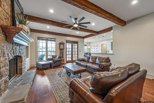 living room with a stone fireplace, dark hardwood / wood-style flooring, ceiling fan, beam ceiling, and french doors