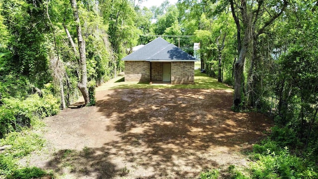 1316 Claude St, Tyler, TX 75702 - view of side of property with an outdoor structure, a view of trees, brick siding, and roof with shingles