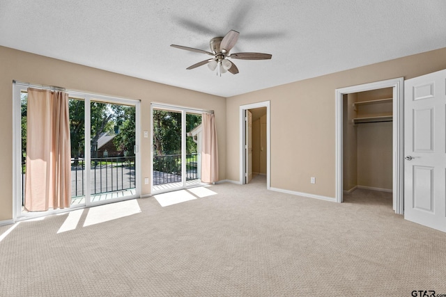 unfurnished bedroom featuring a closet, access to outside, a walk in closet, light carpet, and ceiling fan