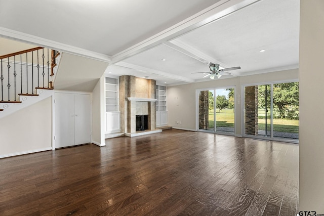 unfurnished living room featuring built in shelves, dark hardwood / wood-style flooring, beamed ceiling, a tile fireplace, and ceiling fan