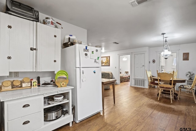 kitchen featuring pendant lighting, hardwood / wood-style floors, light stone countertops, white cabinets, and white fridge