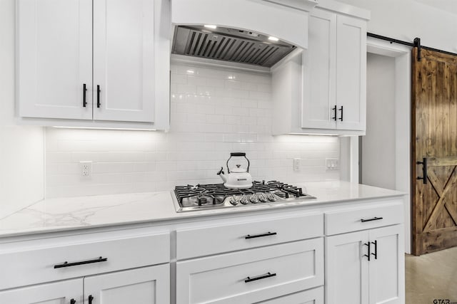 kitchen with stainless steel gas stovetop, ventilation hood, decorative backsplash, a barn door, and white cabinetry