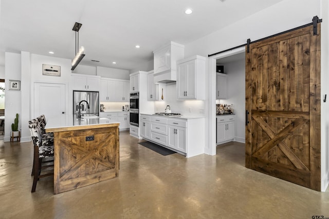 kitchen featuring a barn door, white cabinets, an island with sink, and appliances with stainless steel finishes