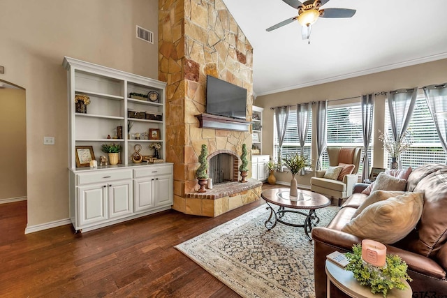 living room with ceiling fan, a stone fireplace, dark hardwood / wood-style flooring, and ornamental molding