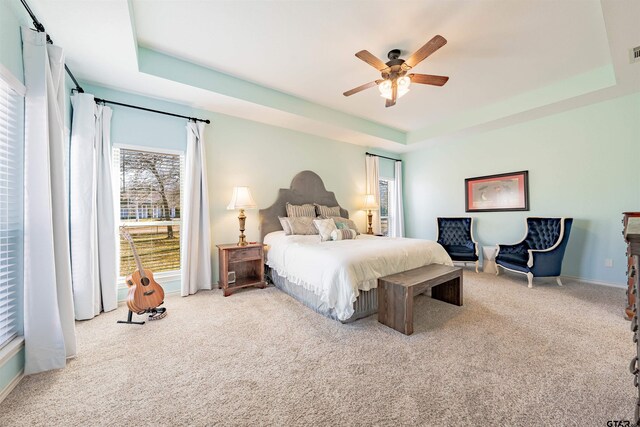 bedroom with ceiling fan, light colored carpet, and a tray ceiling