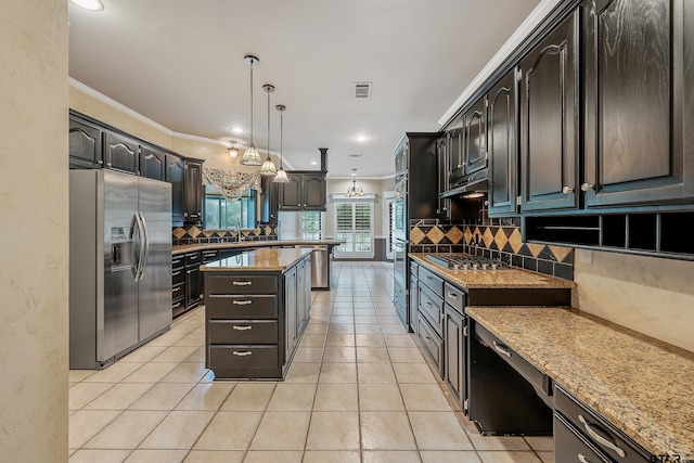 kitchen featuring light stone counters, stainless steel appliances, backsplash, decorative light fixtures, and a center island