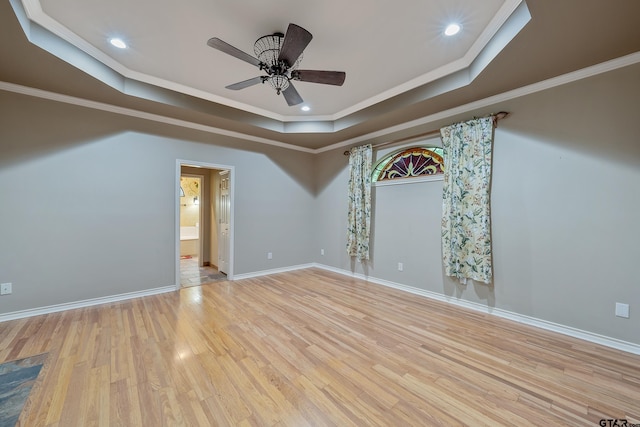 empty room featuring light wood-type flooring, ceiling fan, ornamental molding, and a raised ceiling