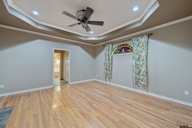 spare room with a raised ceiling, wood finished floors, baseboards, and ornamental molding