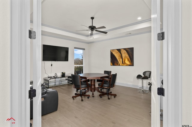 dining space with a raised ceiling, ceiling fan, and light wood-type flooring