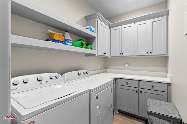 clothes washing area with cabinets, washer and clothes dryer, and light hardwood / wood-style floors