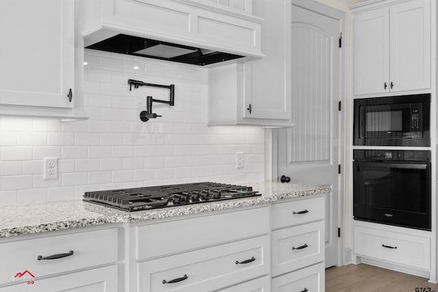 kitchen with light hardwood / wood-style flooring, white cabinetry, light stone counters, black appliances, and custom range hood