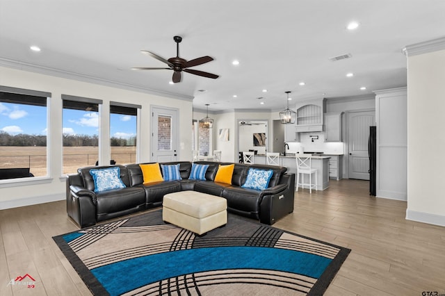 living room with ornamental molding, ceiling fan, and light wood-type flooring