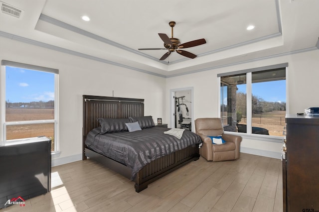 bedroom with ornamental molding, ceiling fan, light wood-type flooring, and a tray ceiling