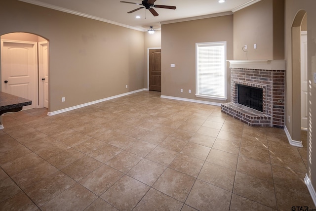 unfurnished living room with a brick fireplace, crown molding, baseboards, and ceiling fan