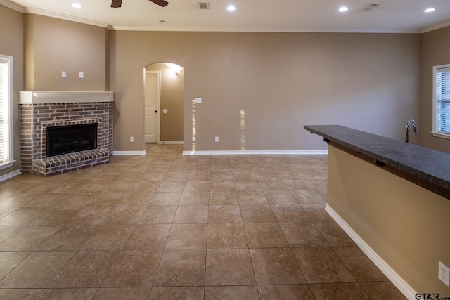 unfurnished living room featuring ceiling fan, baseboards, arched walkways, and crown molding