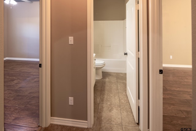 full bath with a tub to relax in, a ceiling fan, toilet, and baseboards