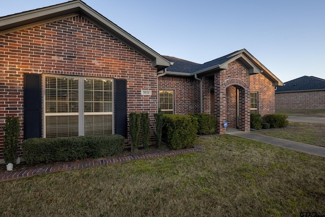 view of front of property featuring a shingled roof, a front yard, and brick siding