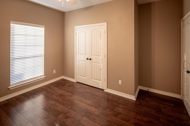 unfurnished bedroom with a closet, dark wood finished floors, and baseboards