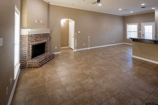 unfurnished living room with crown molding, visible vents, a ceiling fan, a brick fireplace, and baseboards