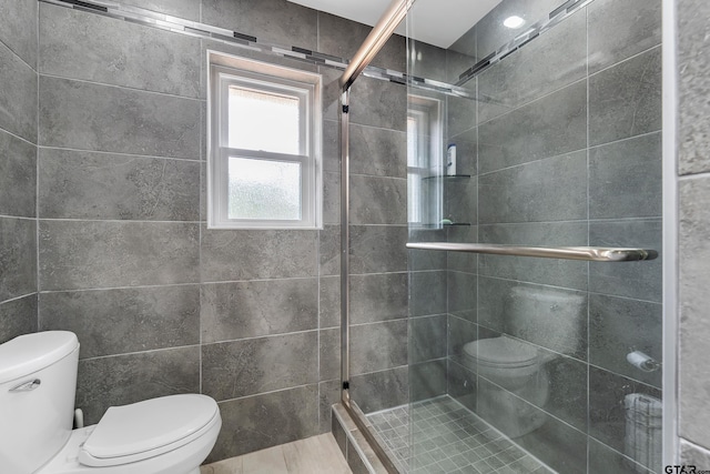 bathroom featuring toilet, tile walls, and a shower with shower door