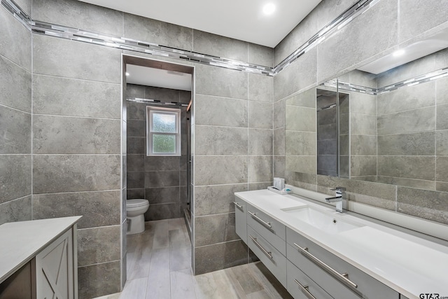 bathroom with wood-type flooring, an enclosed shower, toilet, vanity, and tile walls