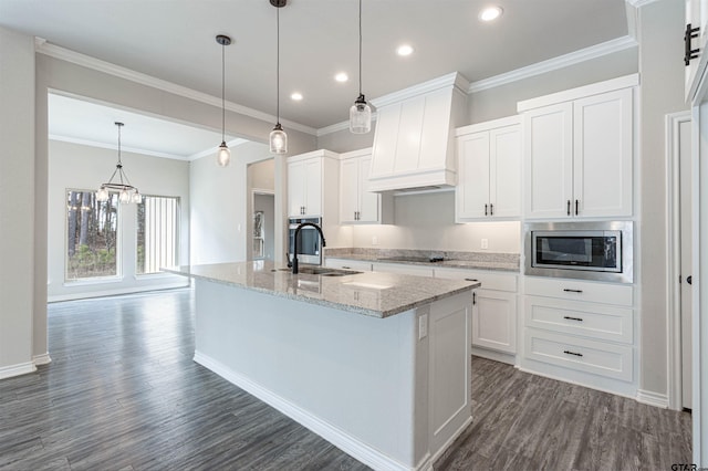 kitchen with custom exhaust hood, an island with sink, stainless steel microwave, sink, and white cabinetry