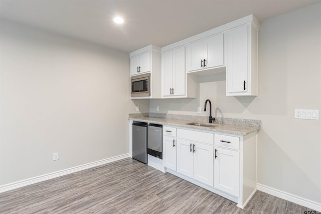 kitchen featuring appliances with stainless steel finishes, white cabinets, light stone countertops, and sink