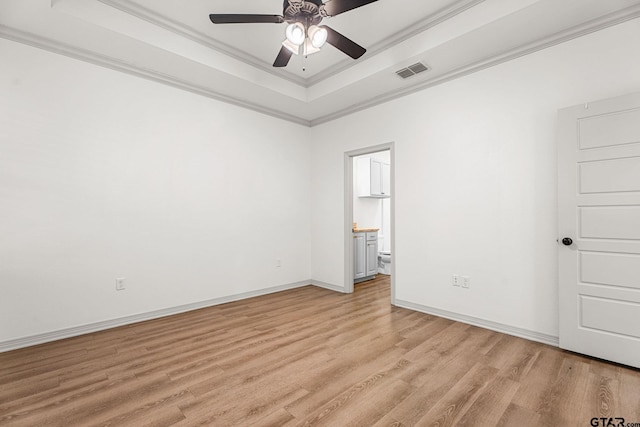 empty room featuring ceiling fan, ornamental molding, a tray ceiling, and light hardwood / wood-style flooring