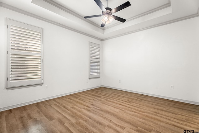 empty room with crown molding, a tray ceiling, ceiling fan, and light wood-type flooring