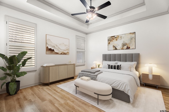 bedroom with ceiling fan, ornamental molding, a tray ceiling, and light hardwood / wood-style flooring