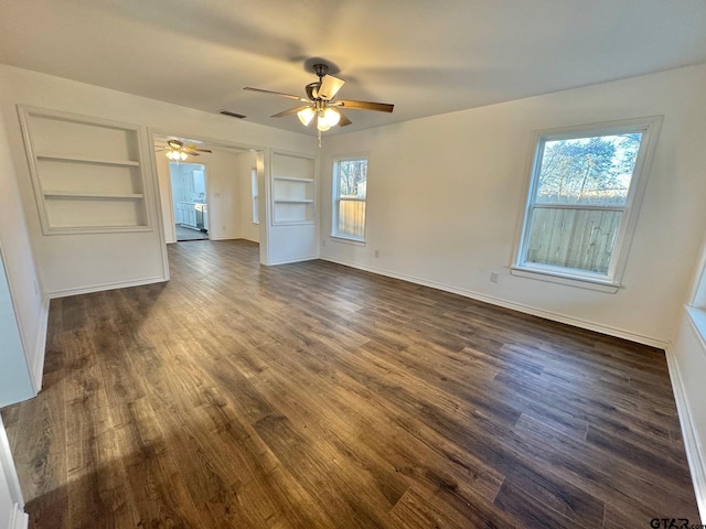 empty room featuring built in features, dark wood finished floors, visible vents, a ceiling fan, and baseboards