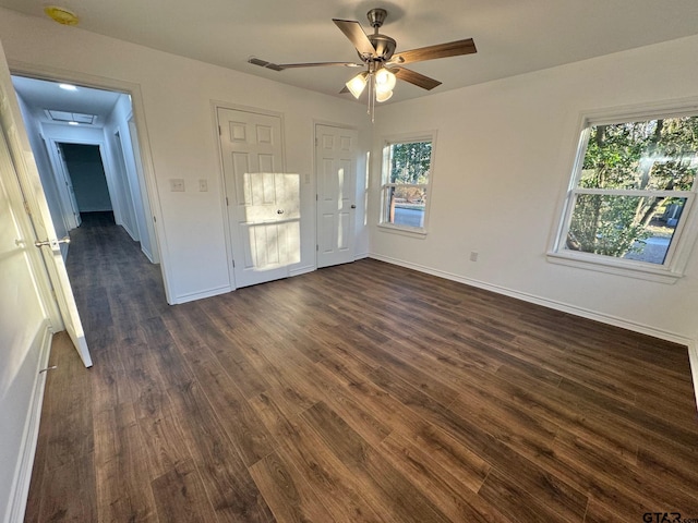 empty room featuring dark wood-type flooring, a ceiling fan, visible vents, and baseboards