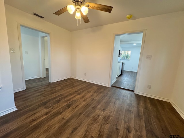 empty room with dark wood-type flooring, visible vents, ceiling fan, and baseboards