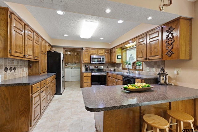 408 E Forest Dr, White Oak, TX 75693 - kitchen with washer and clothes dryer, stainless steel appliances, a textured ceiling, a peninsula, and dark countertops