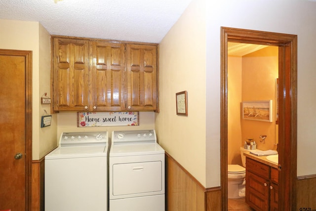 clothes washing area with cabinets, washing machine and clothes dryer, and a textured ceiling