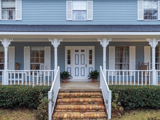 entrance to property with covered porch and a shingled roof