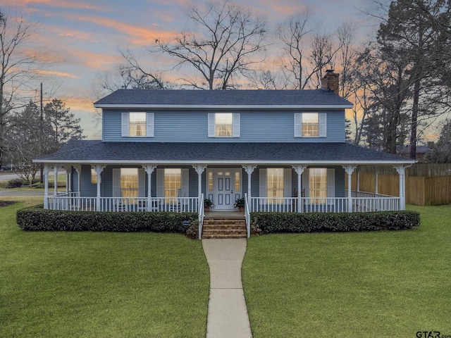 farmhouse with a porch, a front yard, and roof with shingles