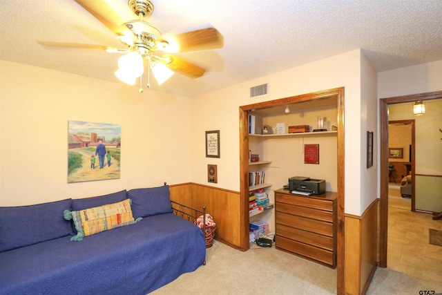 carpeted bedroom with ceiling fan, wooden walls, and a textured ceiling