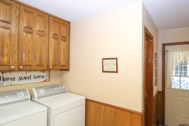 laundry room with cabinets, washing machine and dryer, wooden walls, and a textured ceiling