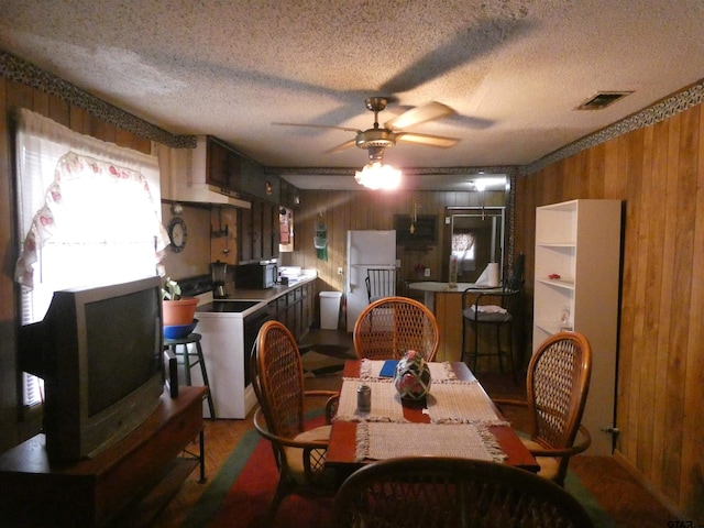 dining space featuring ceiling fan, a textured ceiling, and wooden walls