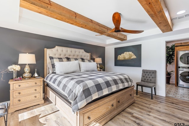 bedroom featuring stacked washer / dryer, ceiling fan, light hardwood / wood-style flooring, and beamed ceiling