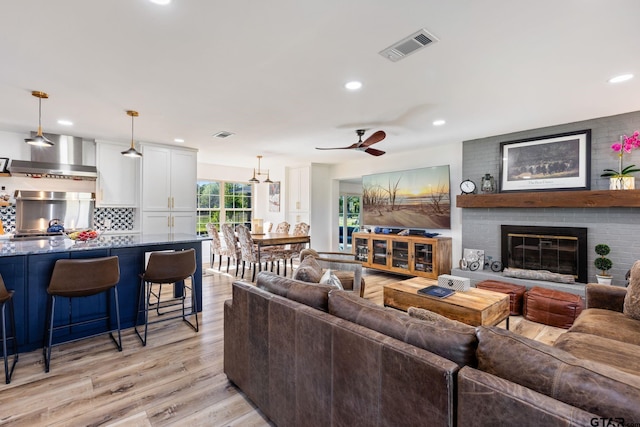 living room with a fireplace, ceiling fan, and light hardwood / wood-style flooring