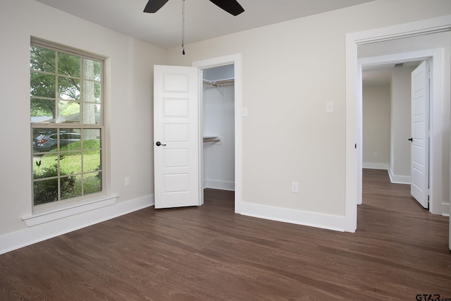 unfurnished bedroom with visible vents, baseboards, a walk in closet, a ceiling fan, and dark wood finished floors